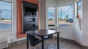 A room with a table and chairs, a large window, and a wall-mounted screen.
