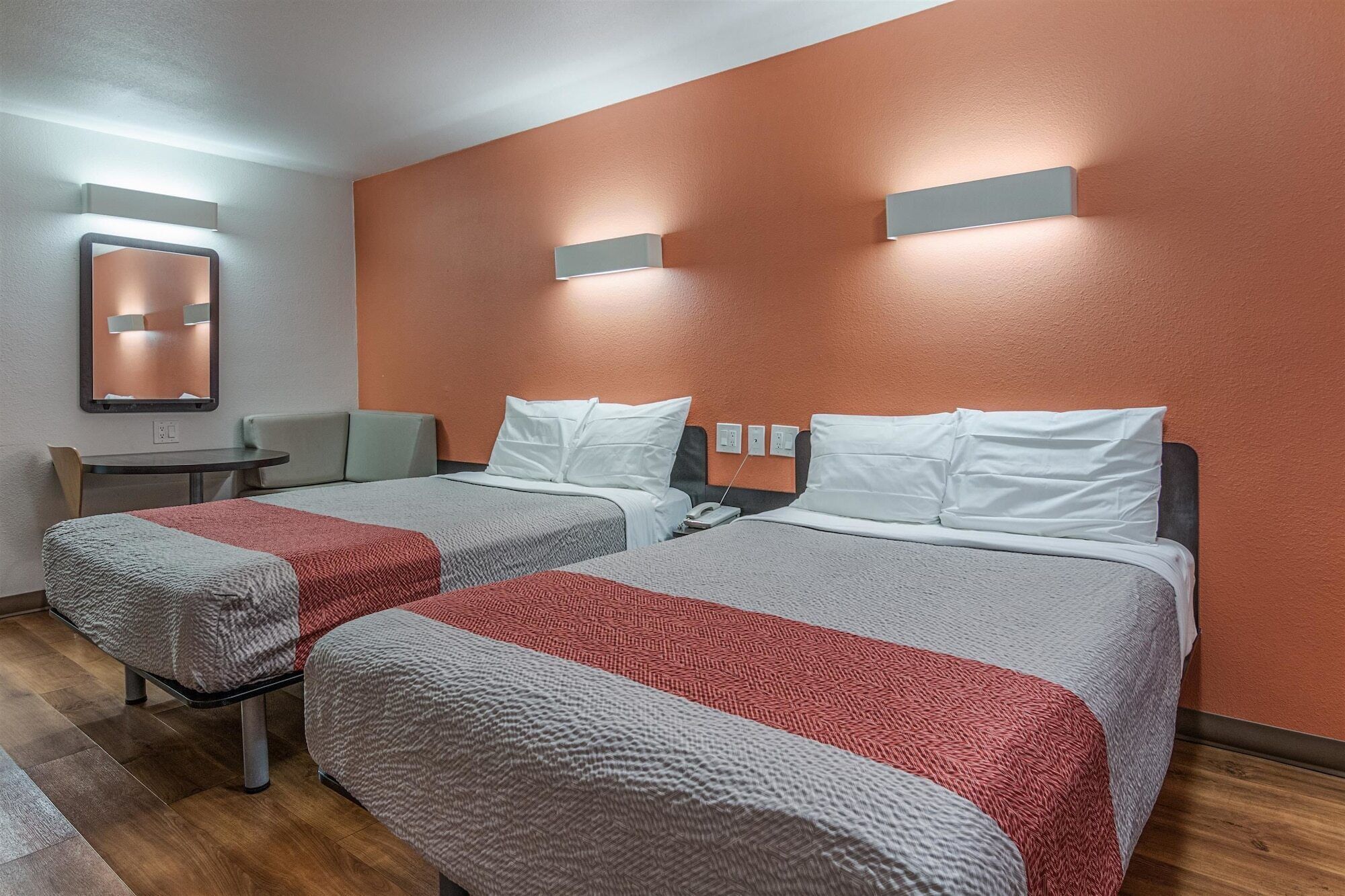 A hotel room with two beds, a small table, a chair, and a mirror.