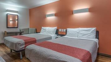 A hotel room with two beds, a small table, a chair, and a mirror.