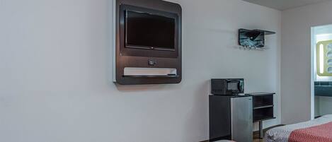A hotel room with a flat-screen TV mounted on the wall, a microwave on a small table, and two beds with patterned bedding.