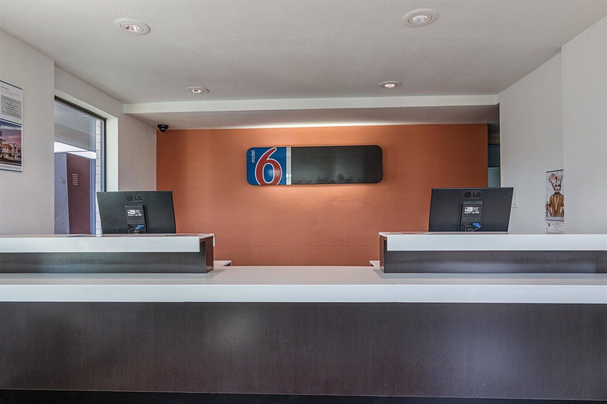 Un mostrador de recepción con dos monitores LG, un cartel grande con el número 6 y una televisión montada en la pared.