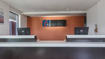 Un mostrador de recepción con dos monitores LG, un cartel grande con el número 6 y una televisión montada en la pared.