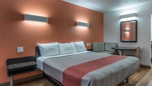A hotel room with a bed, bedside table, chair, and a small table.