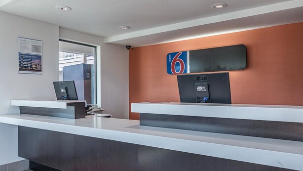 A modern reception desk with a digital screen, a sign indicating room payment, and a view of the outside.