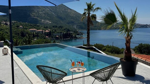 A pool with two chairs and a table, a palm tree, and a mountain view. - Arba Seaview Residences (Zupa dubrovacka)