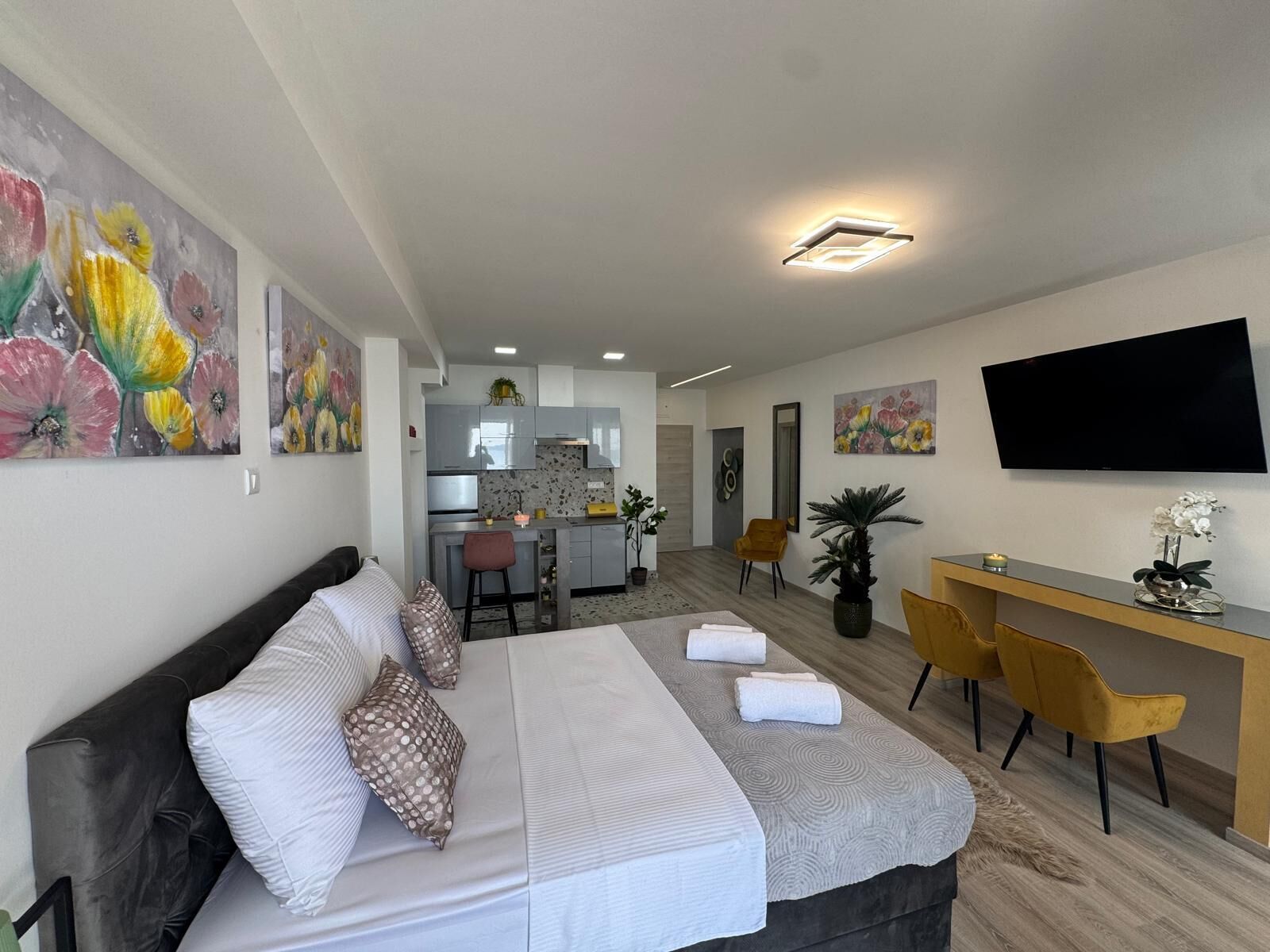 Una habitación de hotel moderna con una cama, un escritorio, un televisor y una cocina al fondo.