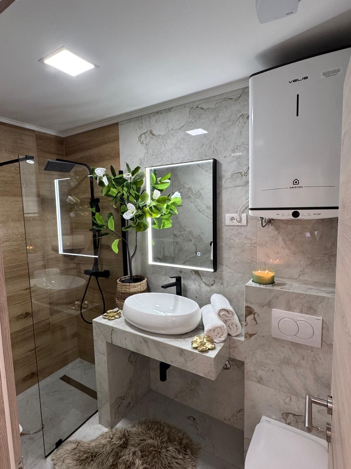 A modern bathroom with a glass shower enclosure, a white sink, a mirror, and a wall-mounted heater.