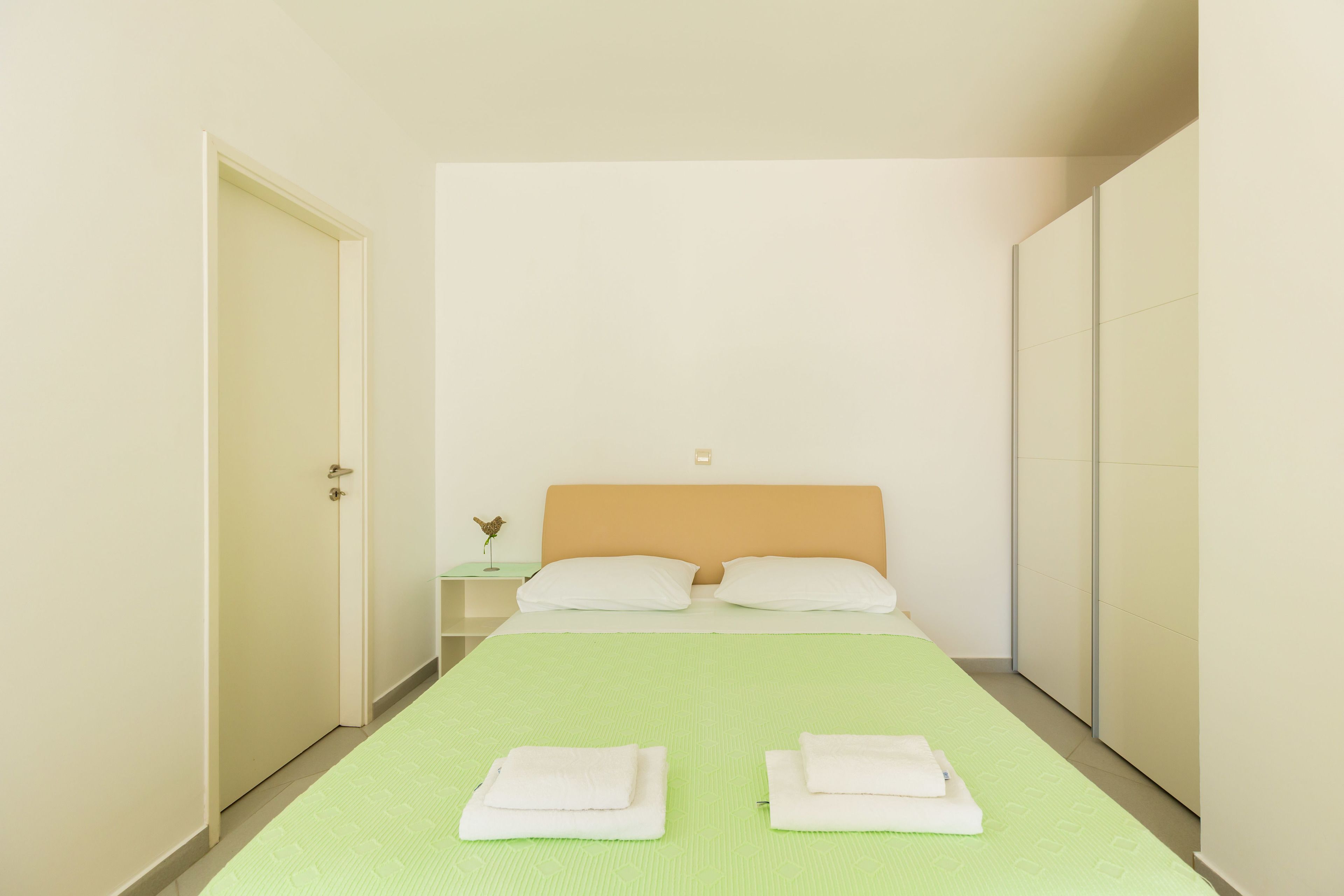 A hotel room with a bed, two pillows, a nightstand, and a green bedspread.
