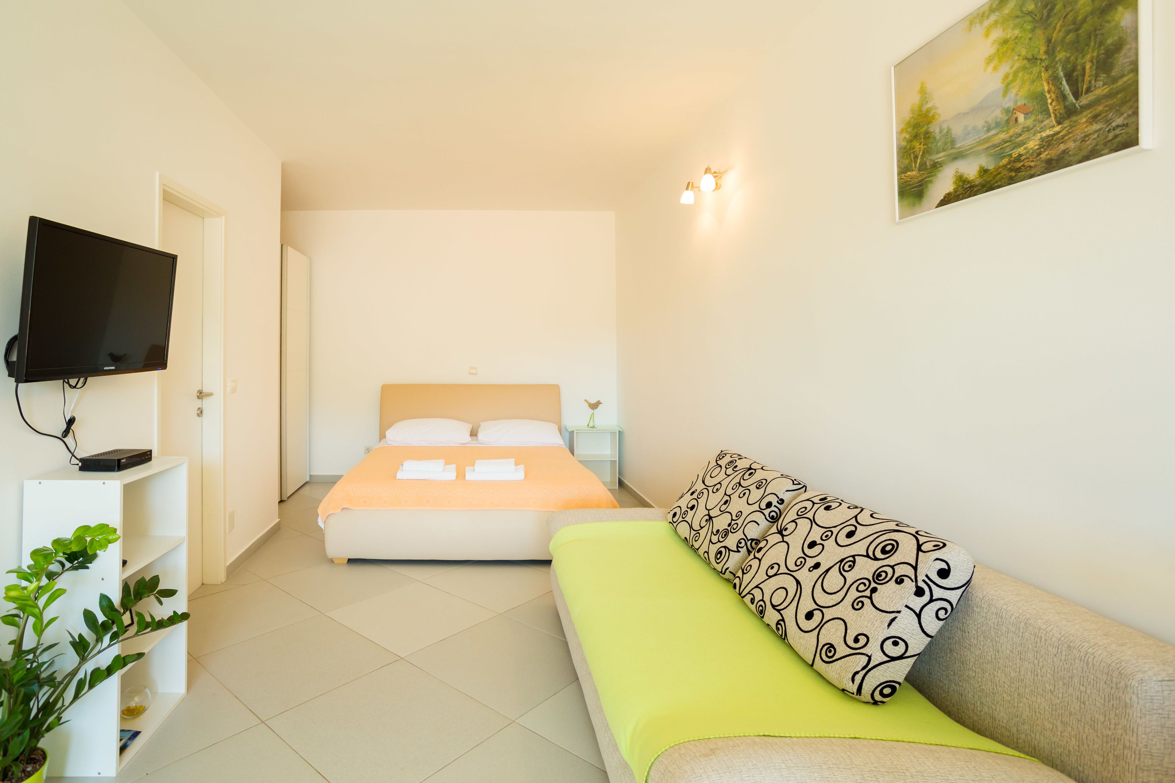 A hotel room with a bed, a sofa, a TV, and a painting on the wall.