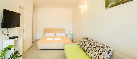 A hotel room with a bed, a sofa, a TV, and a painting on the wall.
