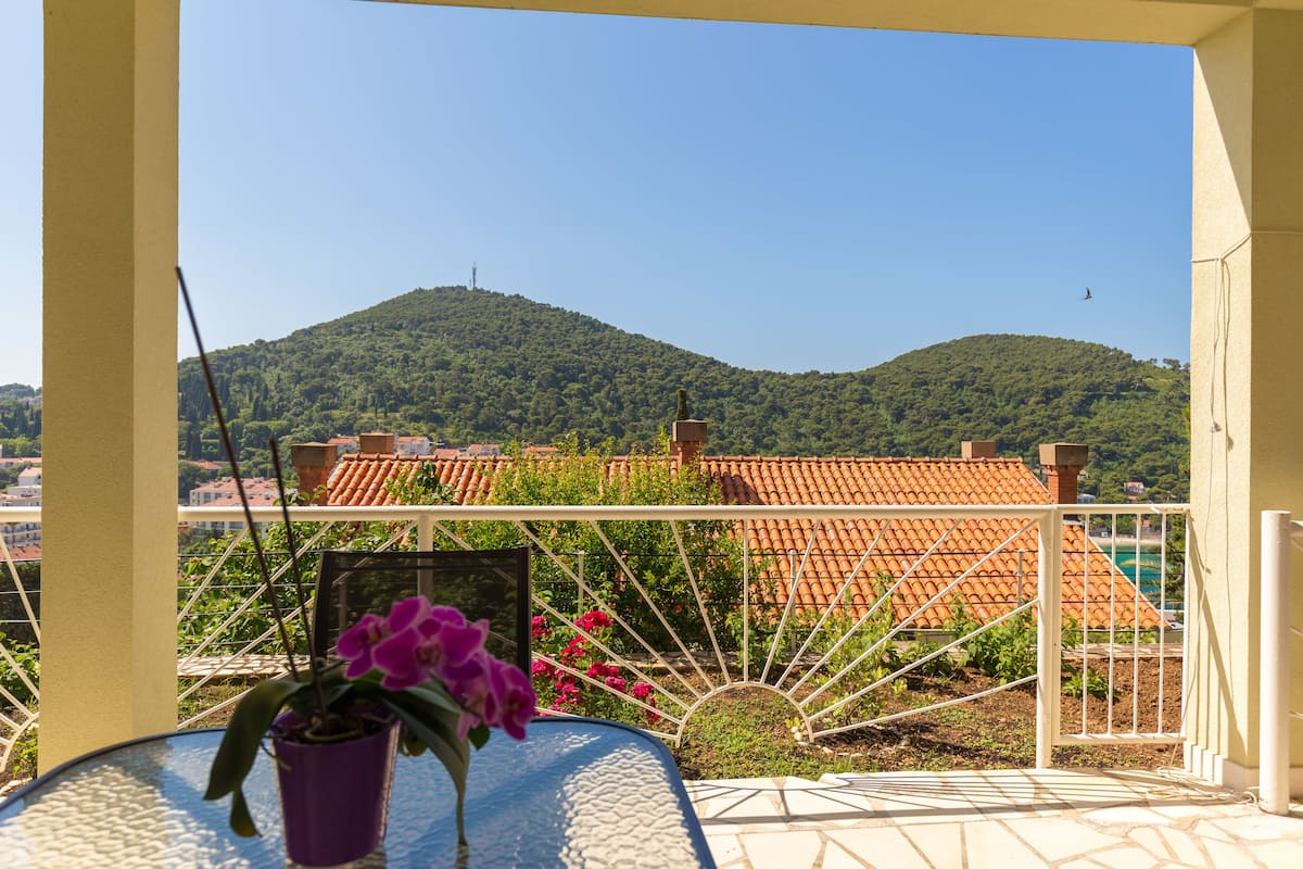 Uma varanda com vista para uma colina, uma mesa com planta em vaso e um parapeito branco.