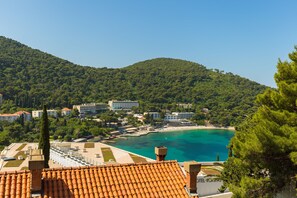 A coastal hotel with terracotta roofs, a beach, and a mountainous backdrop.