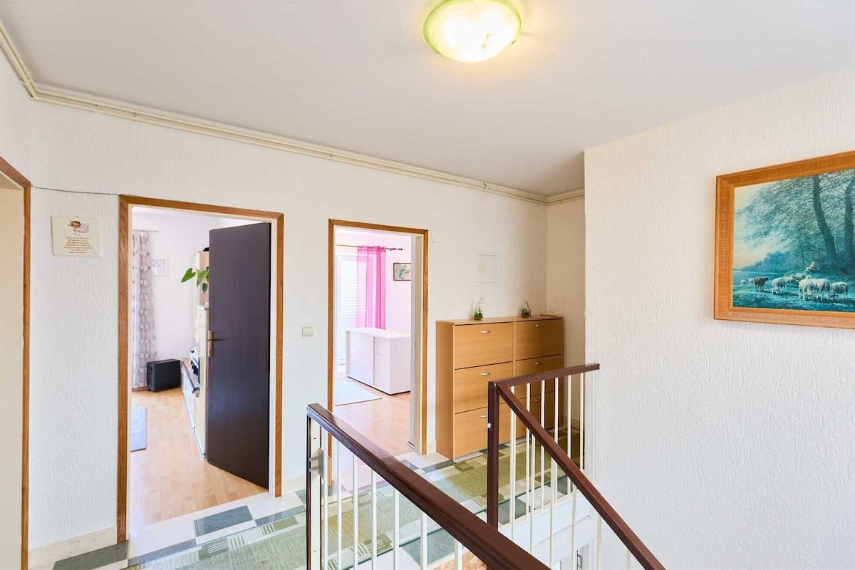 Um corredor com escada, um guarda-roupa de madeira e um quadro emoldurado na parede.