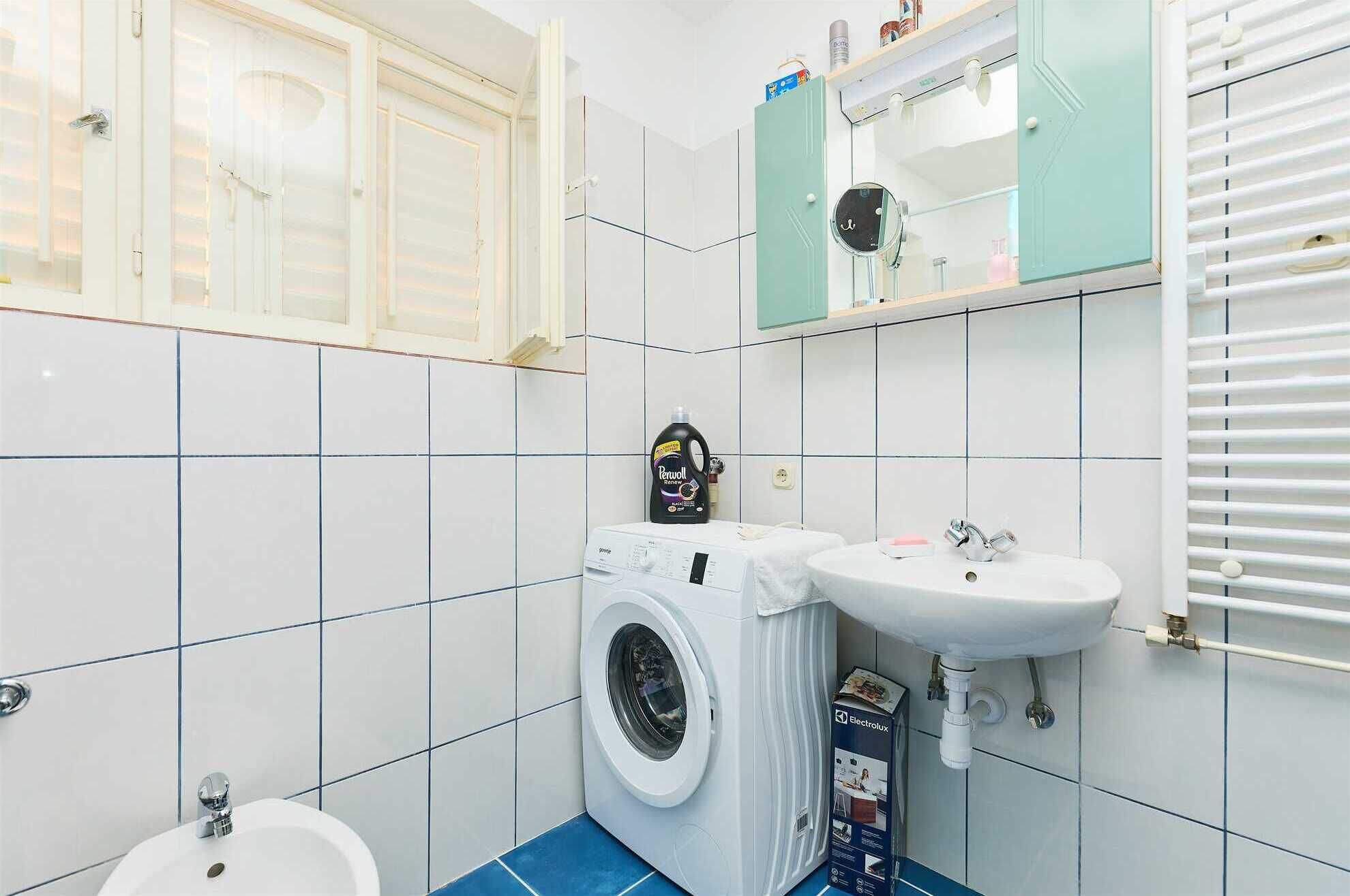 A compact bathroom with a washing machine, a sink, and a toilet.