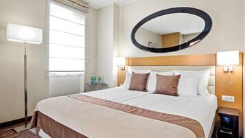 Une chambre d’hôtel avec un grand lit, un grand miroir rond au-dessus, des lampes de chevet et une fenêtre avec des stores.