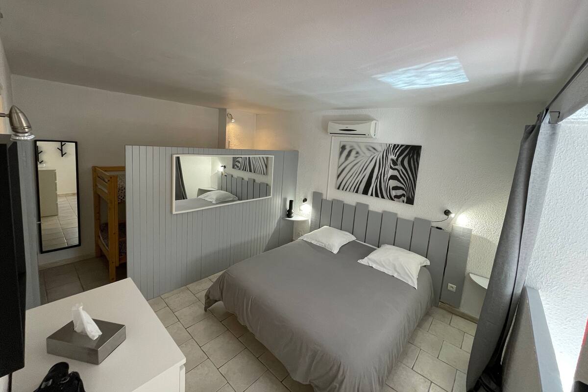 A bedroom with a bed, bedside tables, a mirror, an air conditioning unit, and a zebra artwork on the wall.