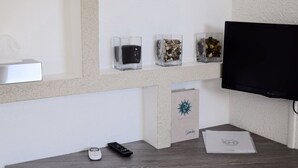 Zona de recepció d'hotel amb un taulell, un televisor i tres recipients de vidre amb diversos objectes a la paret.