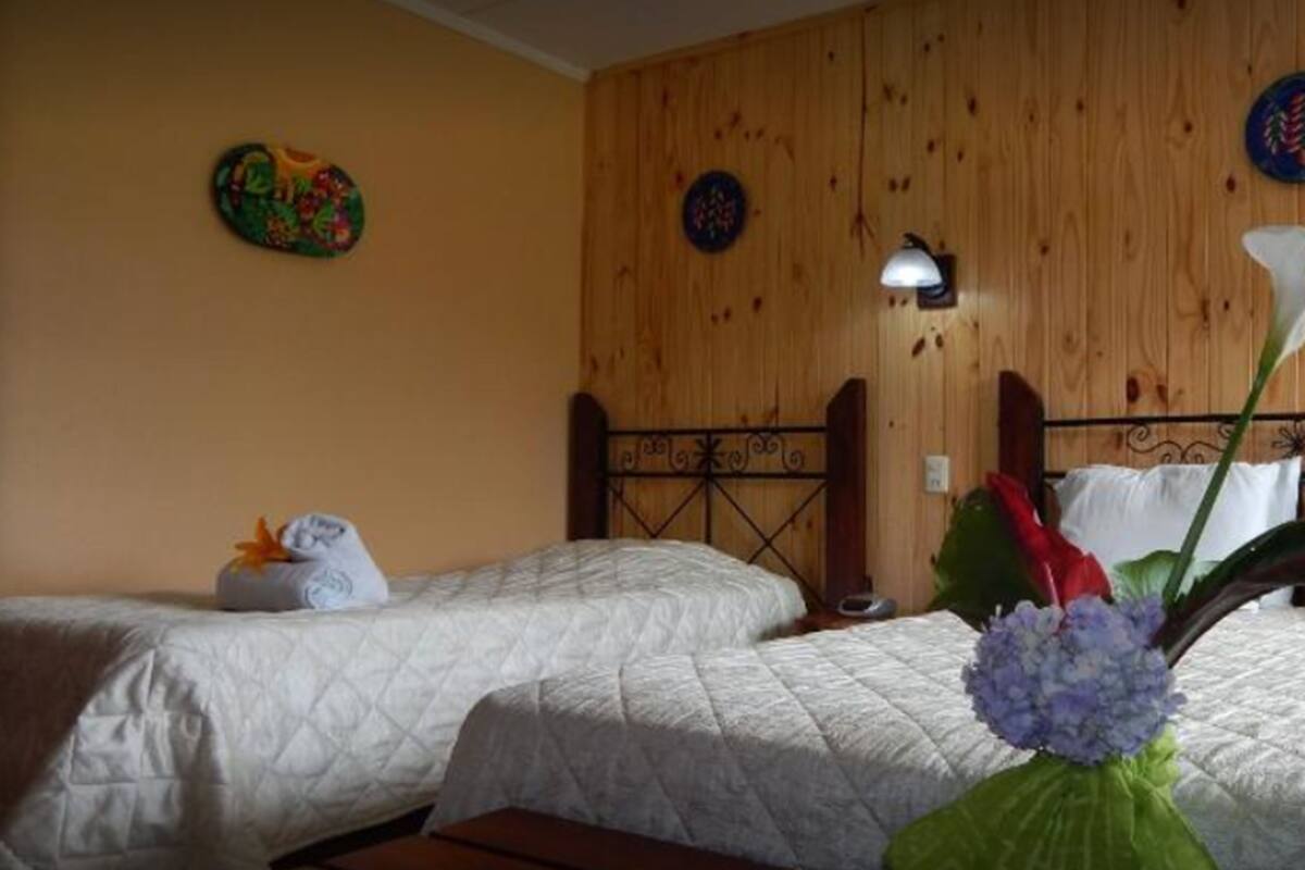 A room with two beds, wooden paneling, a wall clock, and a flower arrangement.