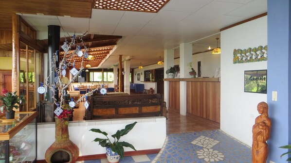 A reception area with a wooden reception desk, a large vase with a plant, and a decorative wall with a framed picture. - Guayabo Lodge (Santa Cruz de Turrialba)