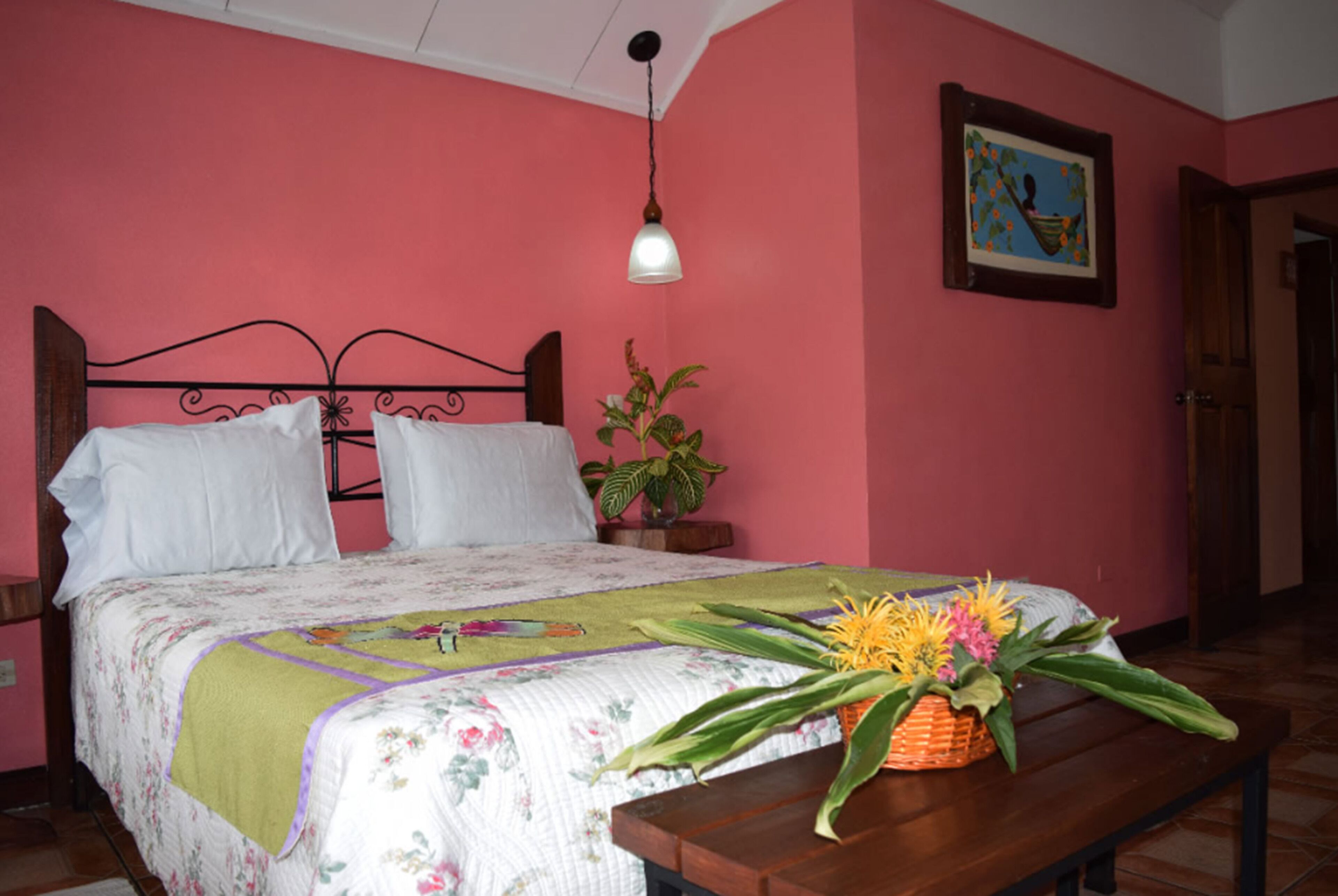 Une chambre à coucher avec un lit, une table de chevet, une lampe, un tableau accroché au mur et une plante en pot.