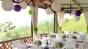 Un espace de restauration en plein air avec des tables dressées pour un repas, des chaises recouvertes de housses blanches et une vue sur un paysage verdoyant.