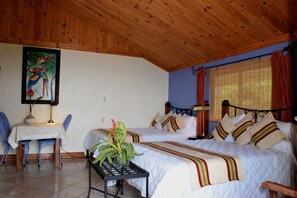 A room with two beds, a dining table, chairs, a small table with a plant, and a painting on the wall. - Guayabo Lodge (Santa Cruz de Turrialba)
