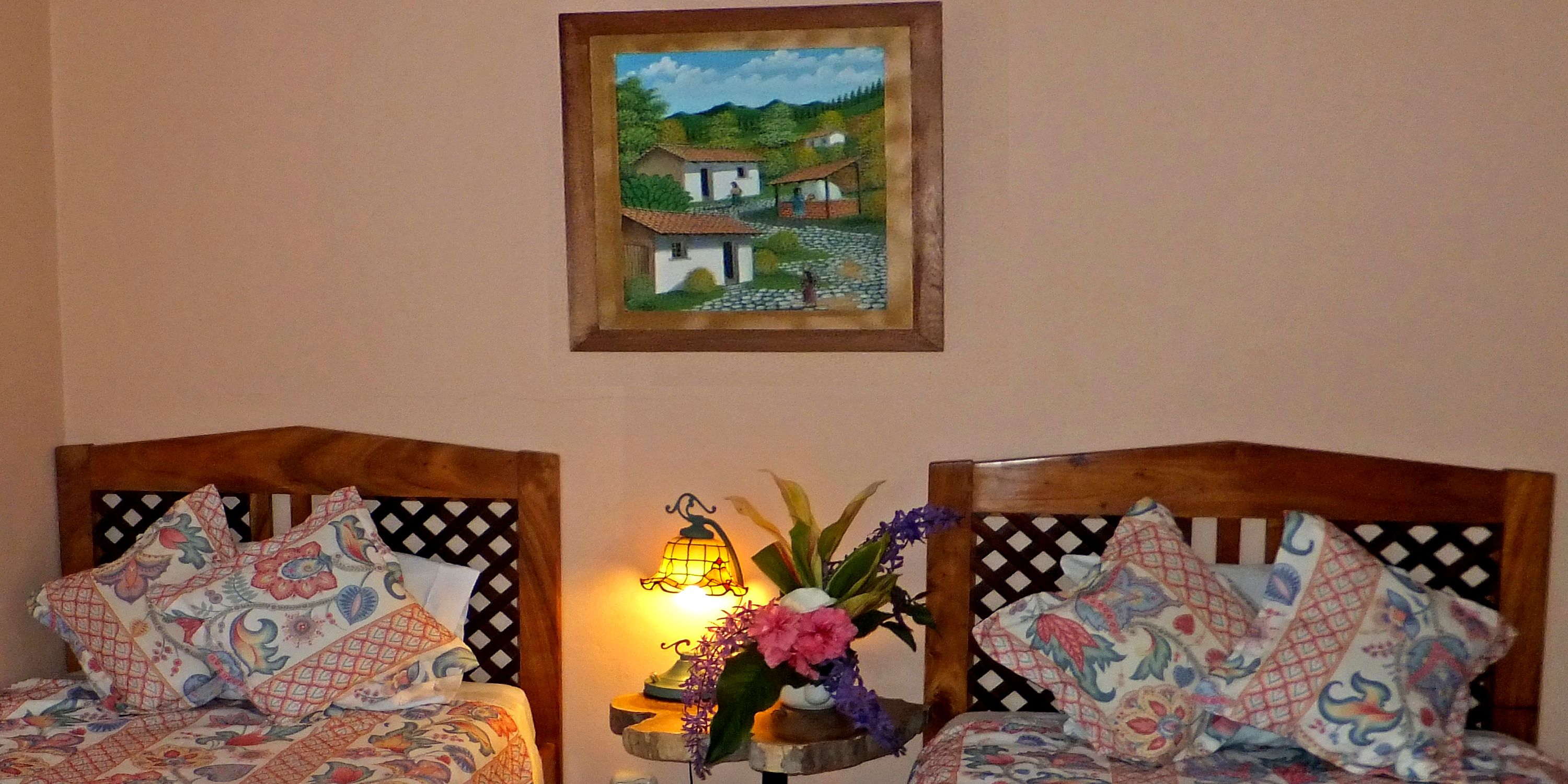 A room with two wooden beds, each with patterned bedding and a decorative lamp between them.