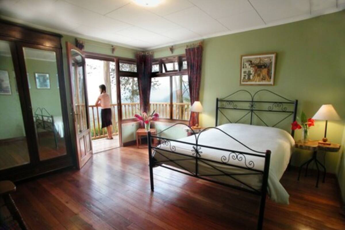 A bedroom with a bed, a chair, a nightstand, a window, and a door leading to another room.