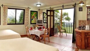 Une chambre d’hôtel avec deux lits, un coin repas, une cuisine et un balcon donnant sur un espace verdoyant.