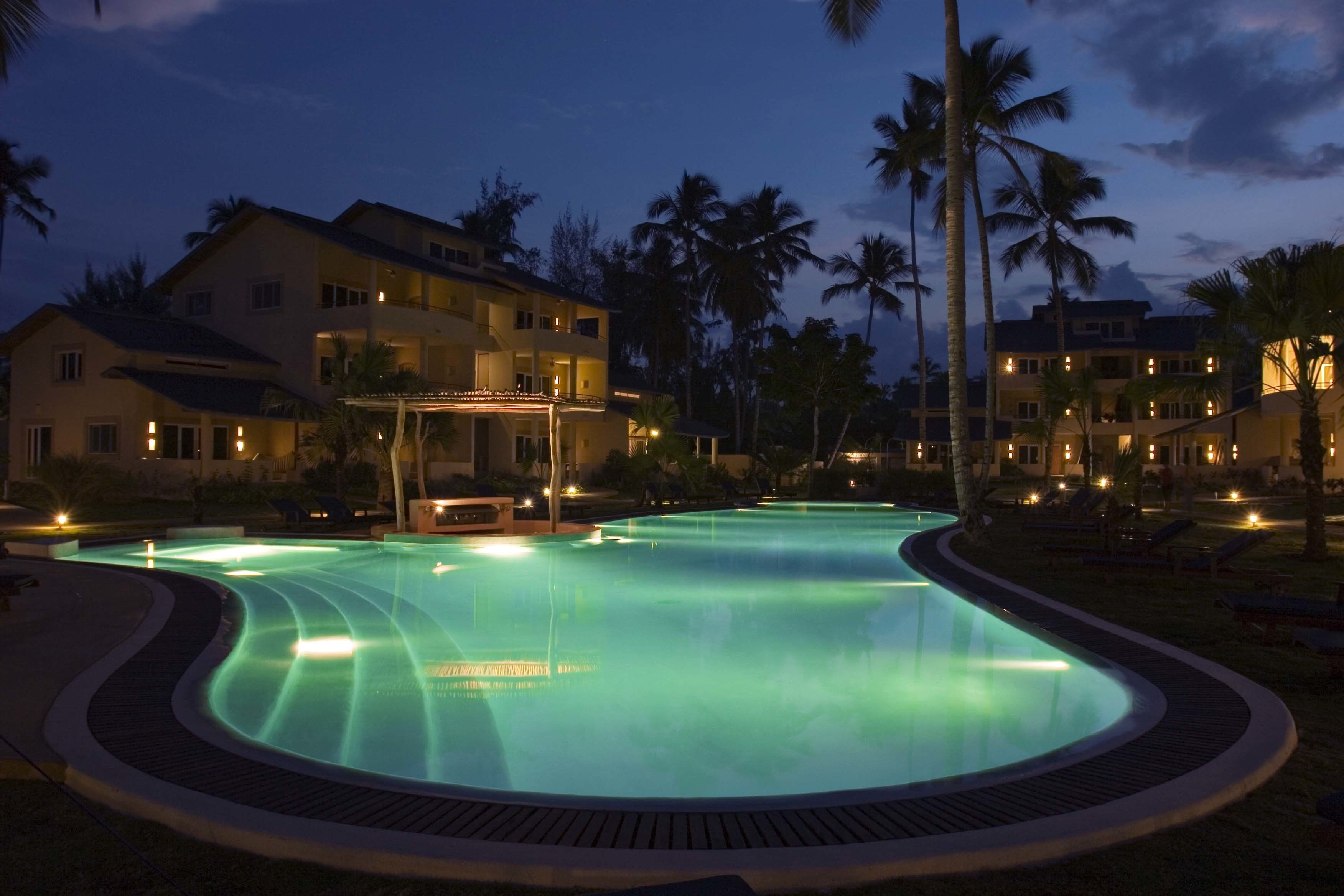 Una piscina de borde curvo, rodeada de palmeras y edificios con balcones.