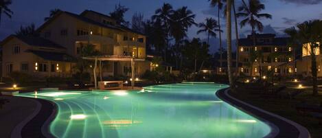 Una piscina de borde curvo, rodeada de palmeras y edificios con balcones.