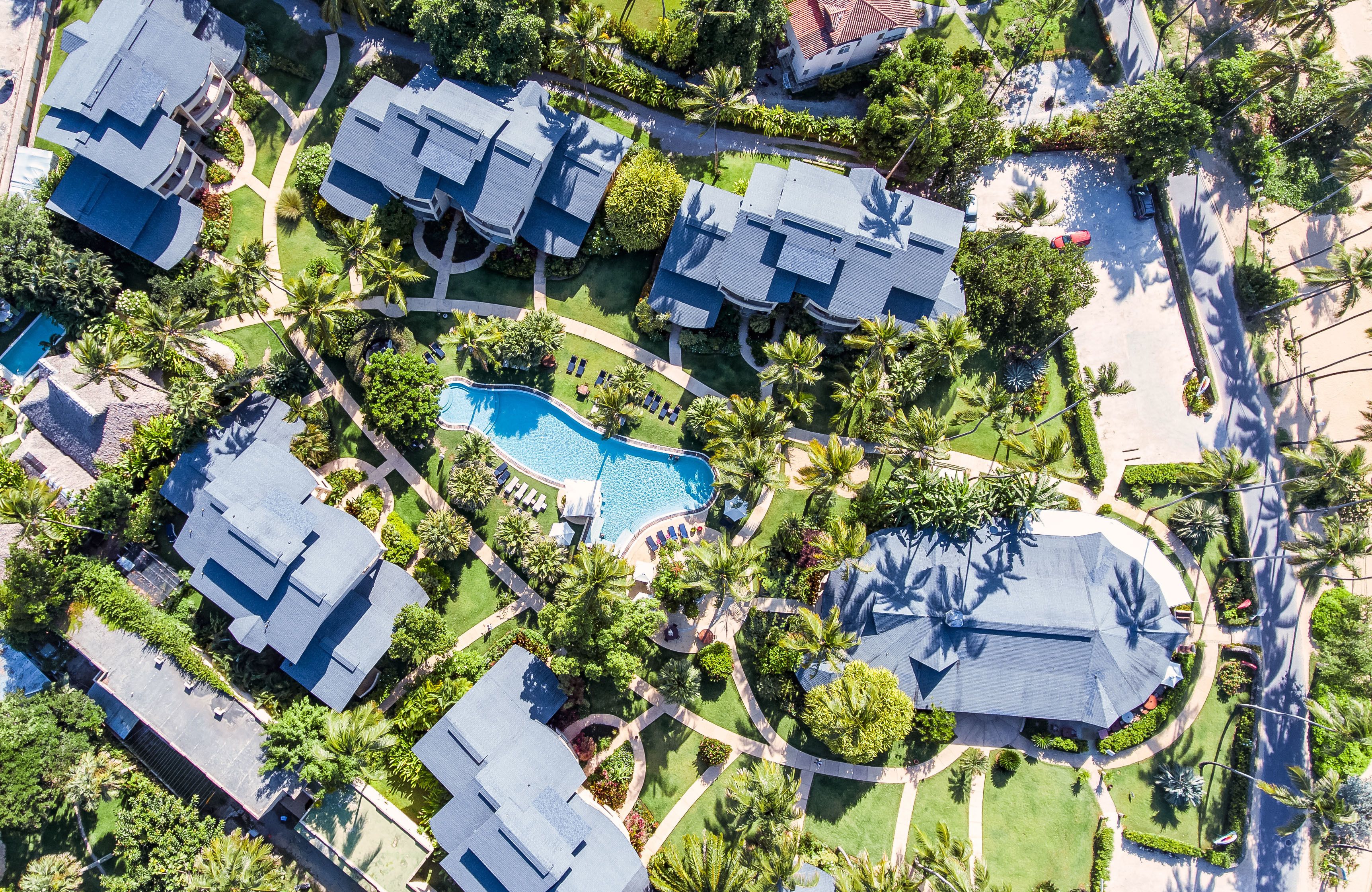An aerial view of a residential area with multiple houses, a swimming pool, and palm trees.