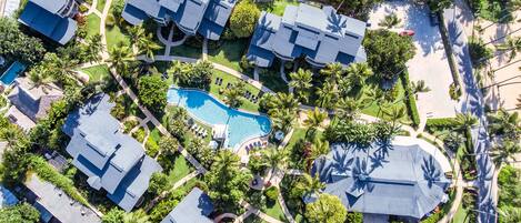 Vista aérea de una zona residencial con varias casas, piscina y palmeras.