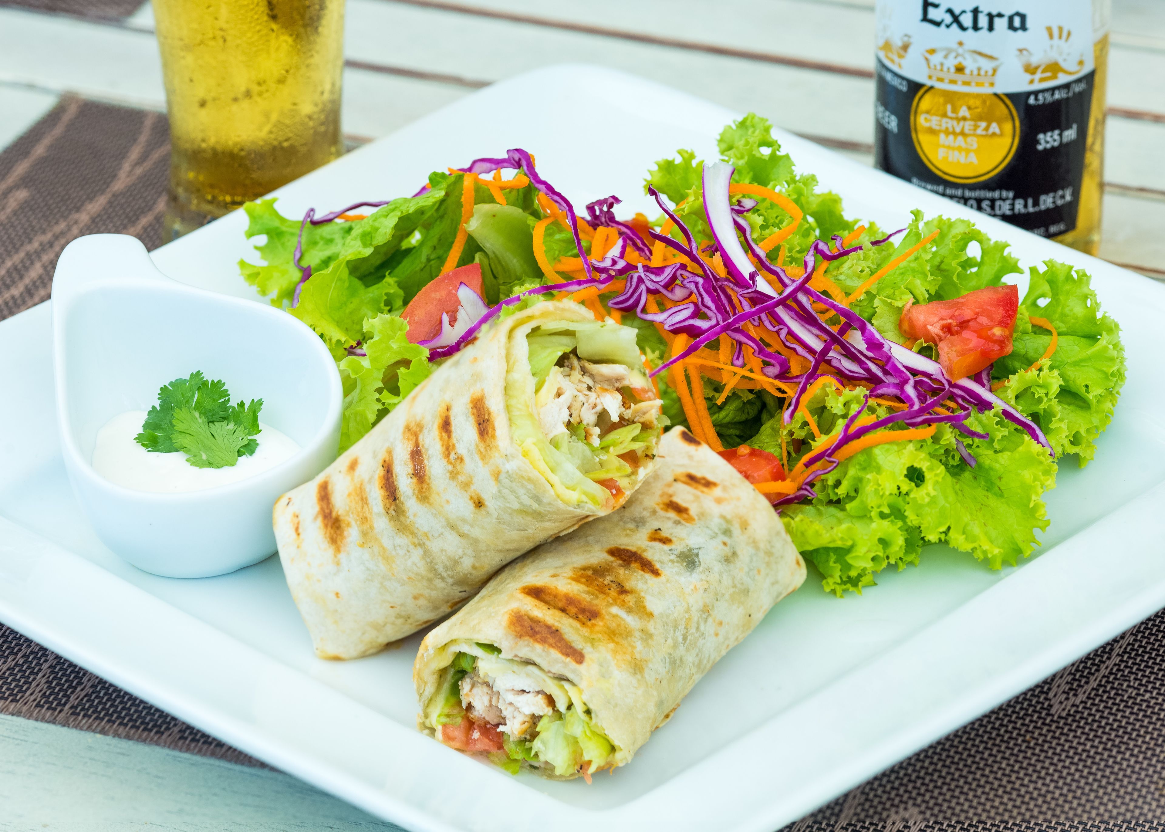 Un plato con un wrap, una ensalada y un recipiente pequeño de salsa.