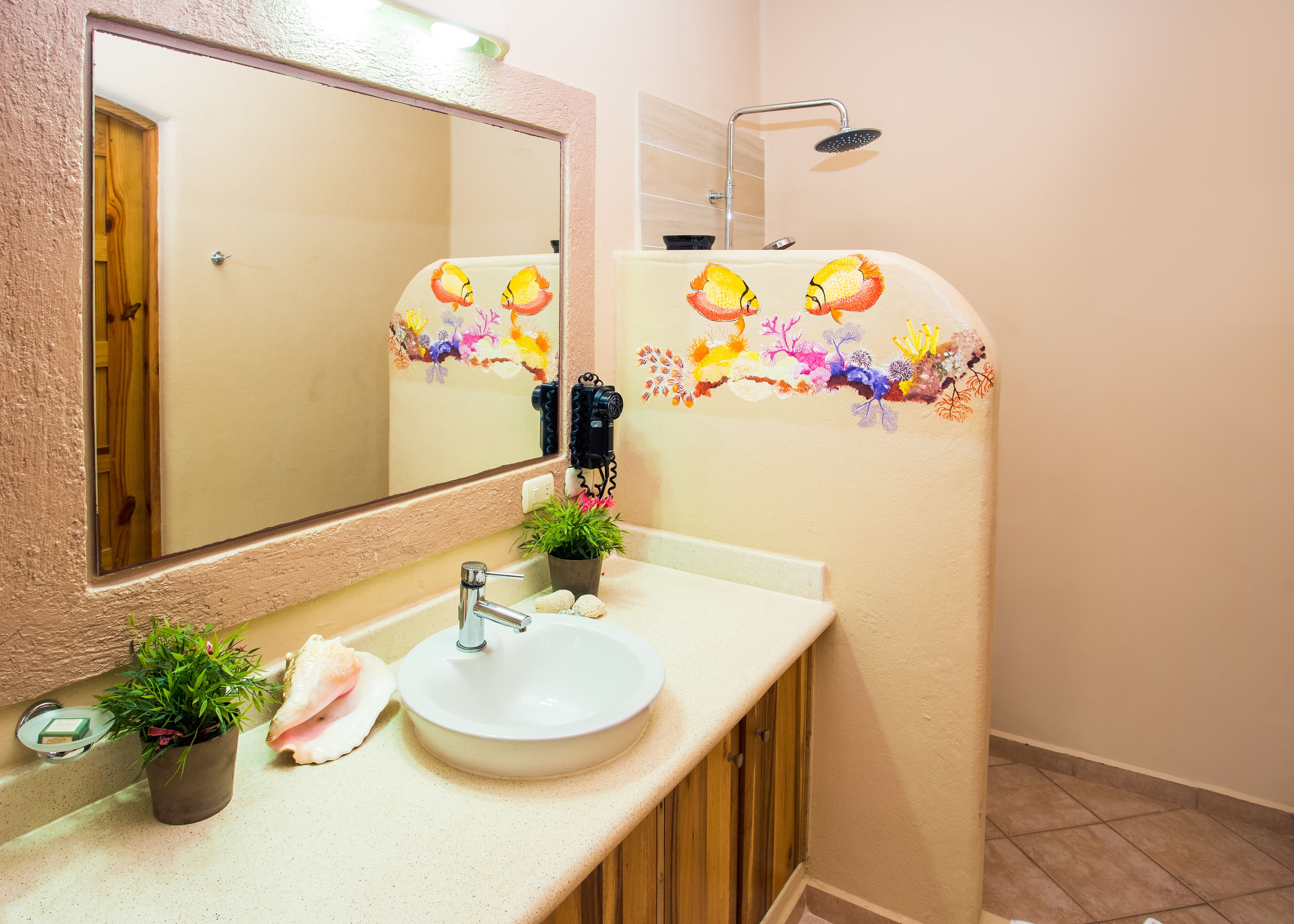 Ein Badezimmer mit Waschbecken, Spiegel und Dusche. Auf der Ablage steht ein Blumentopf und an der Wand sind dekorative Aufkleber.