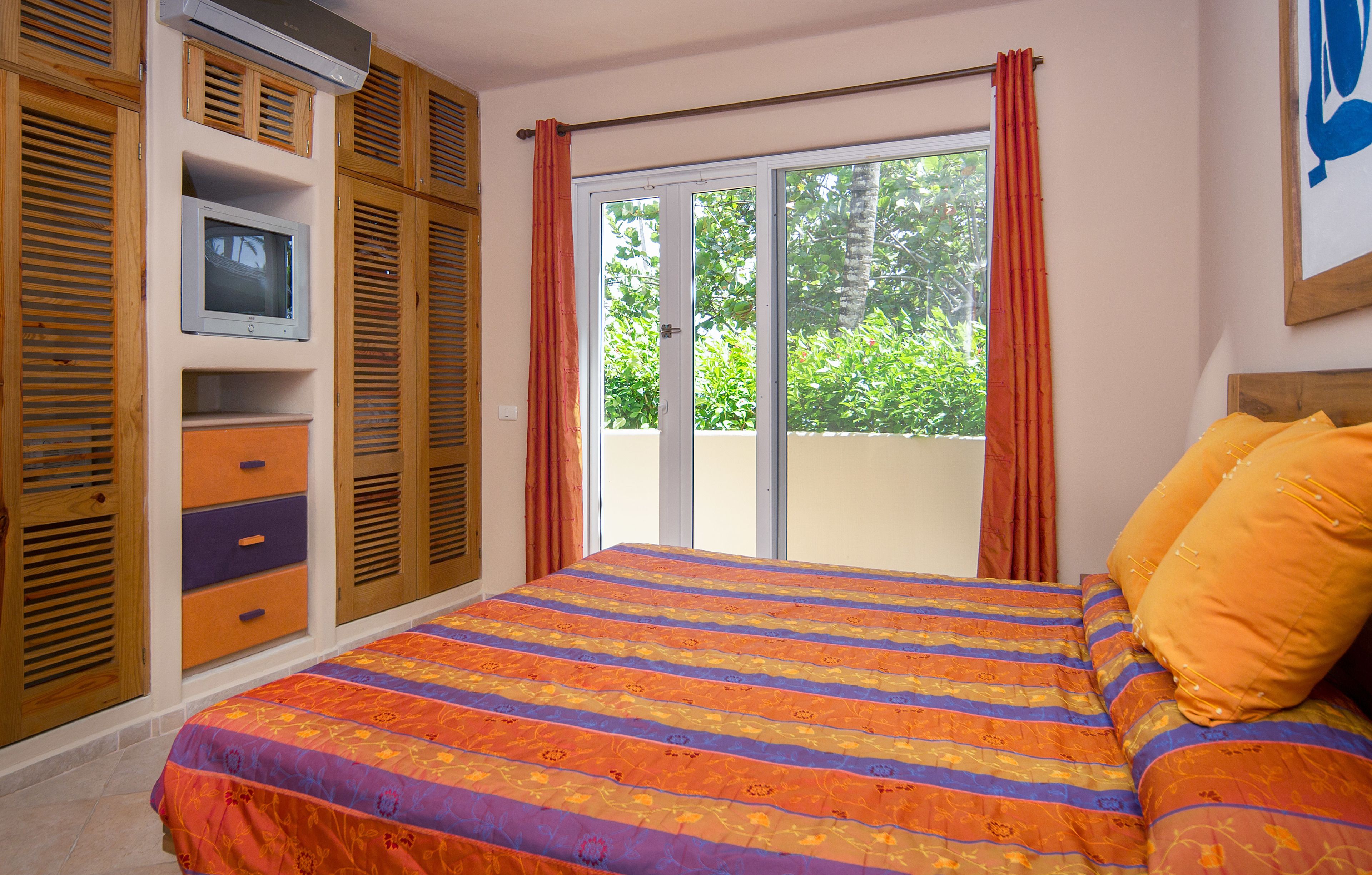 Un dormitorio con cama, televisor y puerta corrediza de cristal a un balcón.