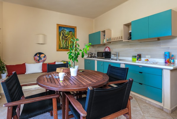 Una cocina compacta con armarios color turquesa, una mesa de comedor de madera y un cuadro en la pared.
