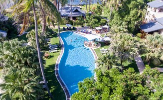 Una gran piscina rodeada de palmeras y sillas de descanso, con vista a un edificio al fondo.