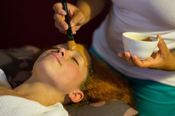 Una persona acostada mientras otra persona le aplica un tratamiento facial.