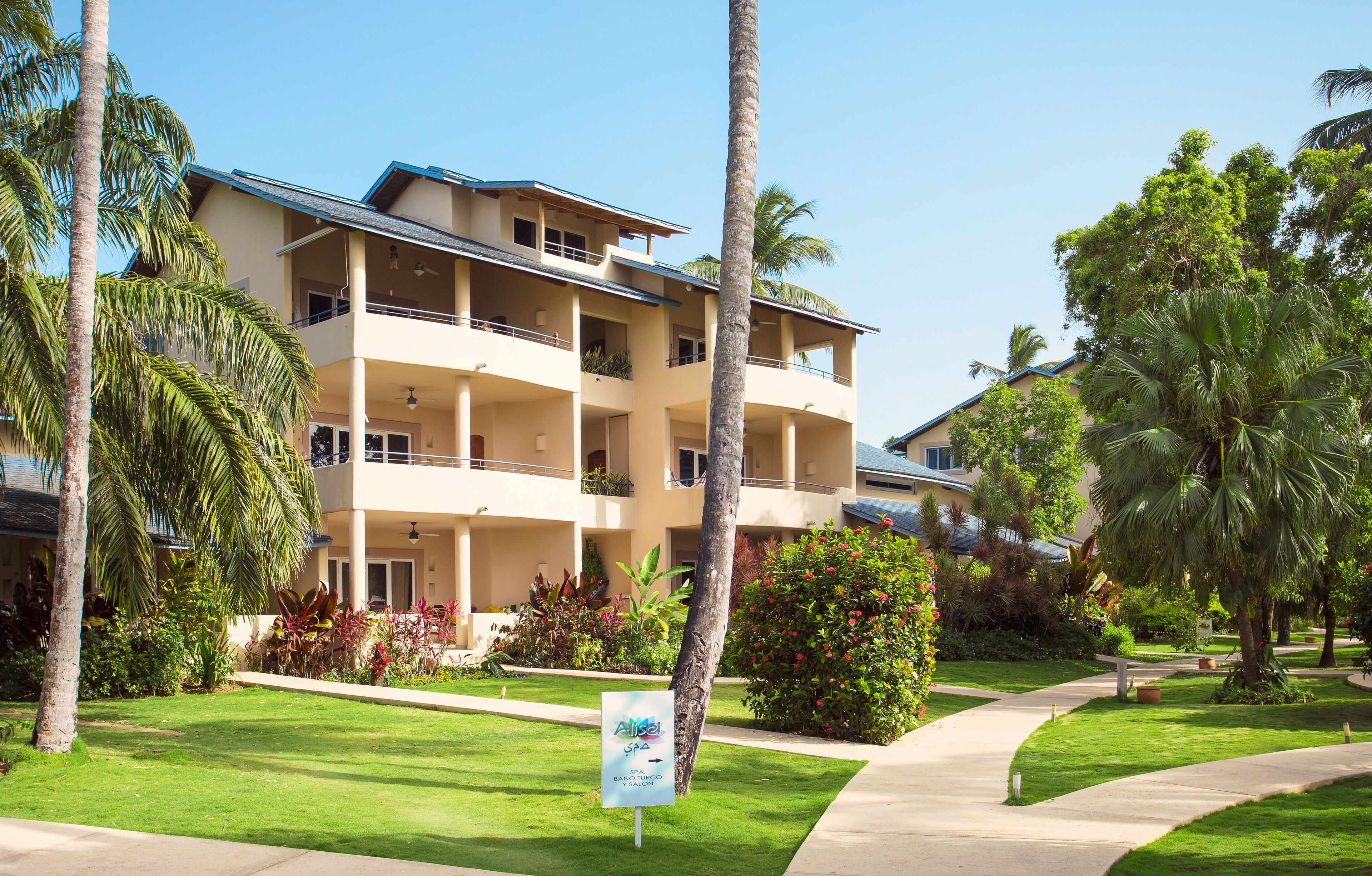 A multi-story hotel with balconies, surrounded by palm trees and well-maintained gardens.
