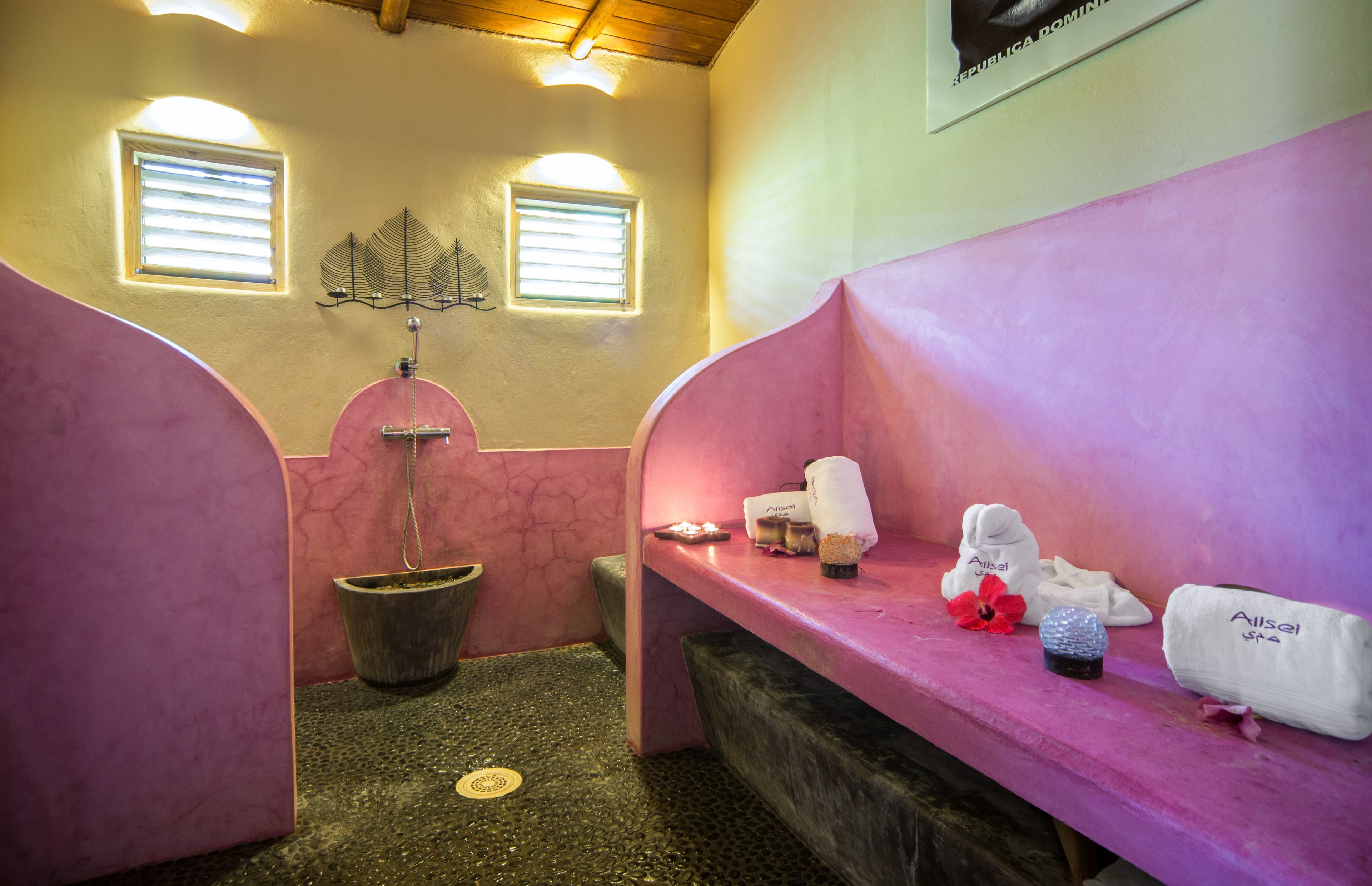 A spa room with two pink benches, a small window, a wall-mounted fan, and a potted plant.