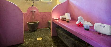 A spa room with two pink benches, a small window, a wall-mounted fan, and a potted plant.