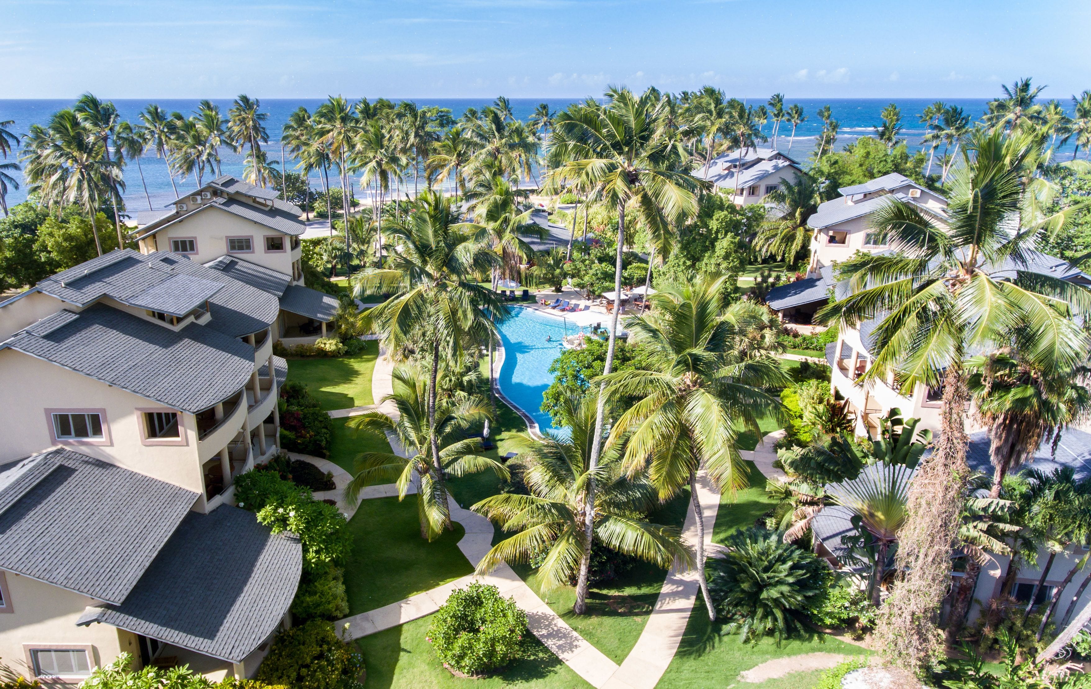 A resort with a central swimming pool surrounded by palm trees and multiple buildings with balconies.