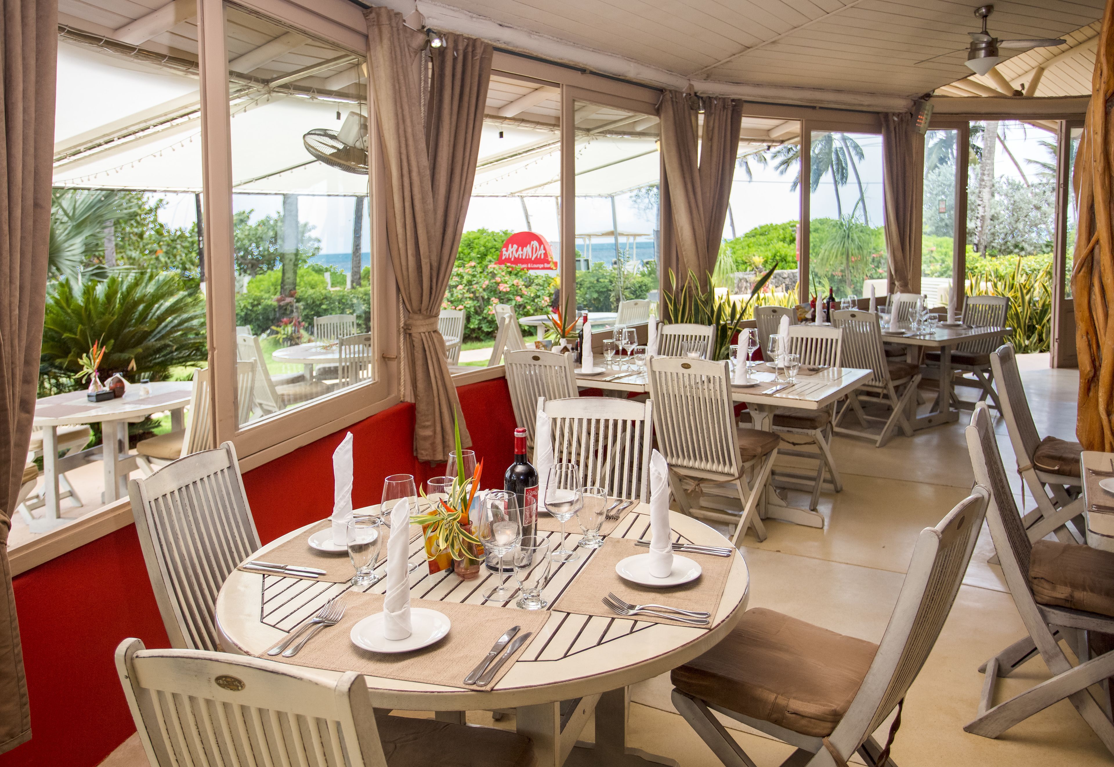 A restaurant with round tables, white chairs, and a view of the ocean.