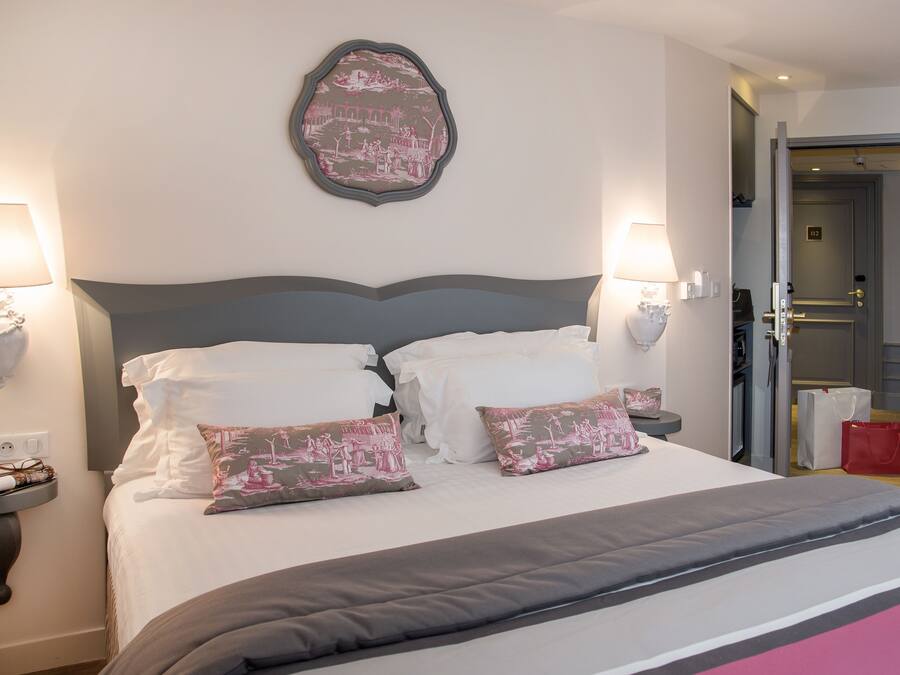 A neatly made bed with white linens and decorative pillows, a wall-mounted artwork, and bedside lamps.