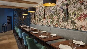A restaurant with long wooden tables, blue chairs, and black pendant lights.