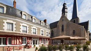A building with a sign reading "LES TROIS MARGANDS" and a church with a tall spire.