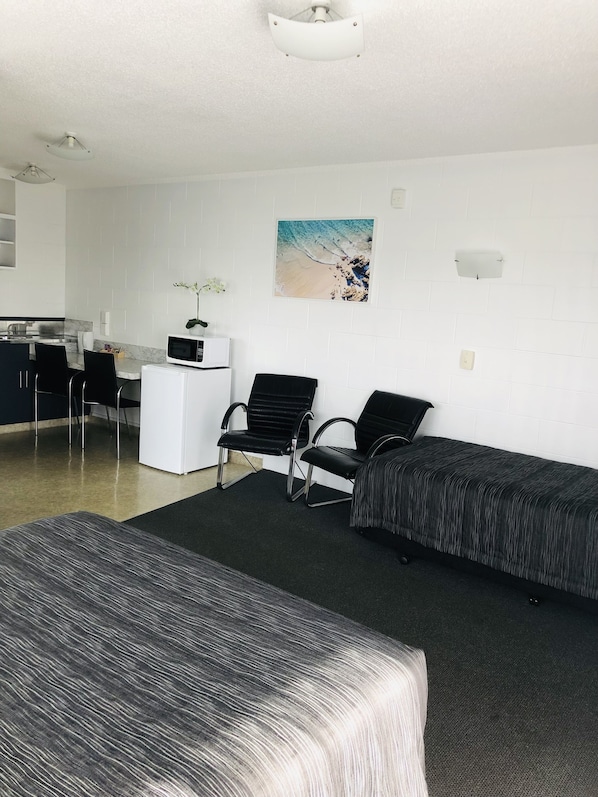 A hotel room with two beds, a kitchenette, a dining area, and a beach-themed wall art. - Blue Haven Motel (Tauranga)