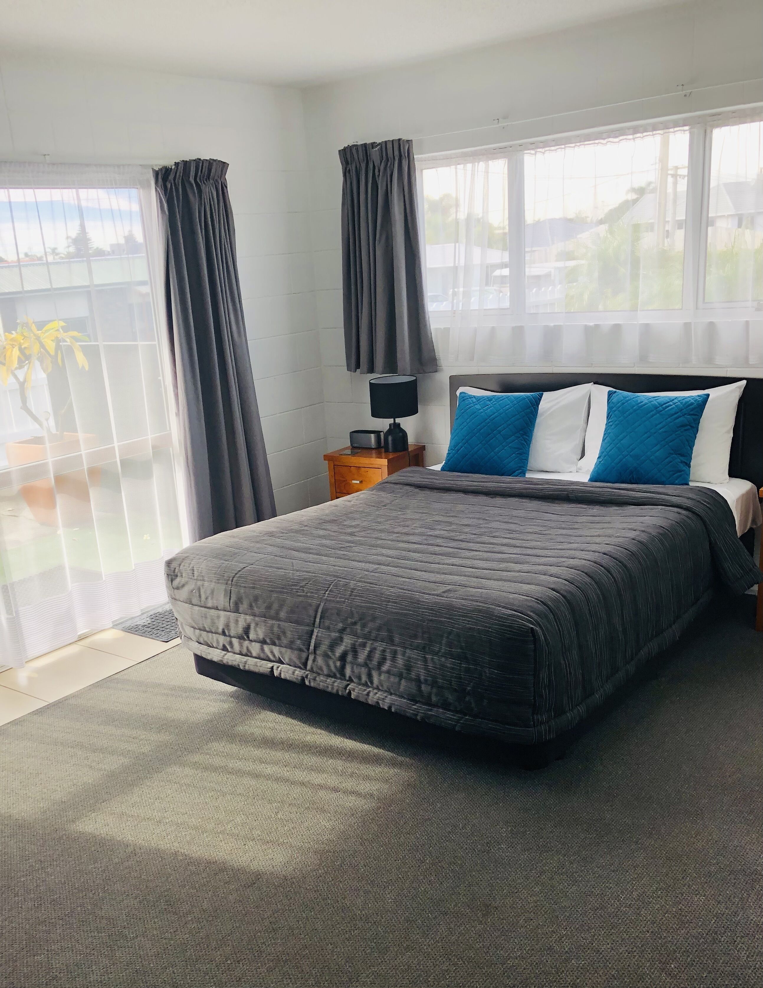 A bedroom with a large bed, a nightstand, a lamp, and a view through the window.
