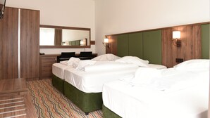 Una habitación de hotel con dos camas, un espejo, un escritorio y un banco tapizado en verde.